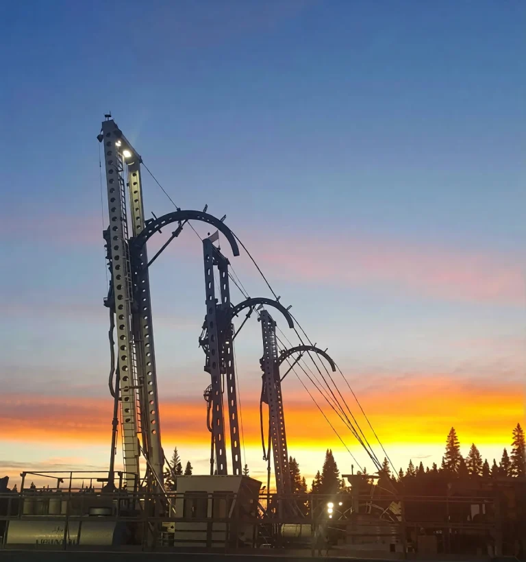 Coiled tubing unit injector masts rigged up on a well site at sunset